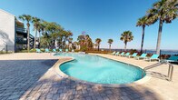 This outdoor pool area in Jacksonville, Florida offers a well-appointed resort-style retreat designed for relaxation and leisure. At its centerpiece is a generously sized freeform pool with crystal-clear blue water, framed by a broad, paver-stone deck that provides ample space for lounging and socializing. Turquoise chaise lounge chairs are thoughtfully arranged around the pool and along the perimeter, inviting residents to soak up the Florida sunshine.

A built-in water feature adds a subtle, elegant touch to the pool's edge, enhancing the tranquil atmosphere. Tall palm trees and mature shade trees are interspersed throughout the space, lending a lush, tropical feel and natural shade. Vibrant tropical plantings with red and green foliage line the fenced boundary, adding color and privacy.

The pool area is enclosed by a black wrought-iron fence that opens toward sweeping waterfront views, creating an impressive backdrop and a seamless connection to the natural surroundings. The adjacent building features covered walkways with distinctive blue architectural accents, adding character to the setting. Well-maintained landscaping with manicured shrubs and greenery borders the walkways, completing the polished, inviting ambiance of this outdoor amenity space.