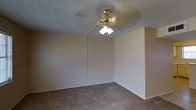 This two-story space in Waco, Texas offers a straightforward and functional layout across two levels. The interior features neutral-toned walls that create a clean, understated backdrop throughout. The room shown is finished with wall-to-wall carpeting in a warm beige-brown hue, providing a comfortable underfoot feel. A textured popcorn ceiling adds a classic residential character to the space, while a brass ceiling fan with an integrated three-bulb light fixture serves as both a practical lighting source and an air circulation solution. The room's clean lines and simple design make it a versatile space easily adaptable to various furniture arrangements. White baseboards provide a crisp contrast against the neutral carpeting and walls. The overall ambiance of the space is calm and move-in ready, with a traditional aesthetic that is well-suited for everyday living. Spanning two floors, the property offers the benefit of separated living areas, allowing for distinct functional zones across its levels. The consistent use of neutral finishes throughout contributes to a cohesive and inviting atmosphere.