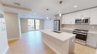 Located at 105 Washington St in Boston's Brighton neighborhood, this well-appointed residence offers four bedrooms and two bathrooms across a single thoughtfully designed floor. Light hardwood flooring runs throughout, lending warmth and continuity to every room.

The open-concept kitchen and living area serves as the heart of the home. The kitchen is outfitted with a large center island featuring a white quartz countertop and undermount sink, stainless steel appliances including a refrigerator, gas range, and microwave, two-tone cabinetry in white and gray, and a classic subway tile backsplash. Pendant lighting above the island adds a refined touch. The adjacent living room receives generous natural light through a large sliding glass door that opens to a private balcony with urban views.

The four bedrooms are comfortably sized, with the primary bedroom offering its own balcony access via a full-length glass door. All bedrooms feature the same light wood flooring and neutral warm tones, with windows providing ample daylight and city views.

The two bathrooms reflect a clean, modern aesthetic. The primary bathroom includes a frameless glass walk-in shower adorned with striking marble-style tile, a floating vanity, and brushed gold fixtures. The second bathroom features a full soaking tub with shower combo and neutral finishes. A hallway and dedicated closet space complete this well-organized layout.