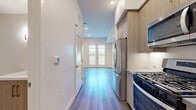 Located at 1340 S Hill St in the heart of Los Angeles' South Park district, this efficiently designed single-floor unit offers a well-planned layout comprising a living room, kitchen, bathroom, and closet. The space features light gray wood-tone flooring throughout the main areas, recessed lighting, and clean white walls that create a bright, contemporary atmosphere.

The living area is open and airy, highlighted by a set of white French doors that invite natural light and provide access to an outdoor space with greenery views — a welcome touch in an urban setting.

The kitchen is a standout feature, outfitted with light wood cabinetry accented by gold hardware, a subway tile backsplash, gray quartz countertops, and a full suite of stainless steel appliances including a gas range, over-the-range microwave, refrigerator, and dishwasher. Upper open shelving adds both function and visual appeal.

The bathroom is clean and modern, finished with large-format light tile flooring, a wood-toned vanity with gold hardware, and crisp white walls. A dedicated closet provides practical storage. A louvered closet door near the entry adds a subtle architectural detail. Smart home controls are visible near the entry, reflecting the unit's modern amenities. Overall, the space presents a polished, move-in-ready environment ideal for urban living.