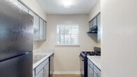 This single-story residence offers a practical and comfortable layout with well-defined living spaces throughout. The galley-style kitchen is efficiently designed with gray cabinetry lining both sides, granite-style speckled countertops, wood-look tile flooring, and a black gas range, refrigerator, and dishwasher. A window at the end of the kitchen allows natural light to filter in, creating a bright workspace.

The living area is notably spacious, featuring vaulted ceilings that enhance the sense of openness. Plush neutral carpet covers the floor, and a window fitted with blinds allows for natural light while maintaining privacy. The vaulted ceiling continues into adjacent areas, adding architectural interest and an airy feel throughout the common spaces. An open archway connects the living area to the kitchen, promoting a cohesive flow.

The bedrooms are generously sized, each carpeted and equipped with windows that bring in natural light. At least one bedroom includes a ceiling fan with a light fixture, adding comfort and functionality. The bathroom features a granite-style countertop vanity, a large framed mirror, and gray cabinetry consistent with the kitchen's design aesthetic, providing a unified look across the unit.