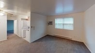 This single-floor unit offers a practical and well-organized layout designed for comfortable everyday living. The living area is carpeted and generously sized, featuring a wall-mounted air conditioning unit, a baseboard heating system, and a window that allows natural light to fill the room. An in-unit stacked washer and dryer is conveniently accessible from the living space, adding a notable level of functionality.

The galley-style kitchen is efficiently arranged with warm-toned wood cabinetry lining both sides, dark granite-style countertops, and white appliances including a refrigerator, electric range, and over-the-range microwave. A window above the sink brings in additional natural light, making the kitchen feel bright despite its compact configuration.

The bedroom is carpeted and features louvered bifold closet doors providing ample storage space, along with a ceiling fan for added comfort. The room is clean and neutral in finish, offering a quiet and restful atmosphere.

The full bathroom includes a tub and shower combination with a curtain rod, a toilet, tile flooring, and a small window for ventilation and natural light. The space is finished in crisp white throughout, maintaining a clean and functional aesthetic.

Overall, the unit presents a straightforward, move-in-ready layout with all essential amenities thoughtfully incorporated into the space.