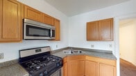 This single-floor unit offers a practical and functional layout across several well-defined rooms. The kitchen is equipped with warm honey-toned wood cabinetry, granite-style countertops, a corner double-basin stainless steel sink, a gas range, and an over-the-range stainless steel microwave. Light tile flooring completes the kitchen's clean, utilitarian aesthetic.

The living spaces consist of multiple rooms finished with wall-to-wall carpeting in neutral tones. Several of these rooms benefit from multiple windows that invite generous natural light and provide outdoor views of surrounding greenery and streetscapes. One room features a ceiling fan with integrated lighting, adding to comfort and airflow. Crisp white walls throughout lend a bright, airy feel, while classic white trim and baseboards add a touch of architectural detail. One room also showcases decorative molding above the windows, hinting at the building's character.

The full bathroom is finished with light travertine-style tile flooring and includes a shower-tub combination, a toilet, and a wood-vanity with a countertop sink. White walls and chrome fixtures keep the space clean and functional.

Overall, this single-floor unit presents a straightforward, well-maintained living environment with consistent finishes and ample natural light throughout.