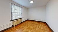 Located at 51 E Church St in Martinsville, Virginia, this one-bedroom, one-bathroom unit offers a thoughtfully arranged single-floor layout comprising a living room, bedroom, kitchen, bathroom, and hallway. Throughout the space, warm hardwood flooring is a consistent and defining feature — with classic parquet patterns in the living area and straight-laid planks in the bedroom and hallway — lending a sense of continuity and character.

The living room receives natural light through large windows fitted with horizontal blinds, and cast-iron radiators provide a nod to the building's heritage. The bedroom is a comfortable size, featuring the same rich hardwood floors, a window overlooking the surroundings, and a radiator below it. Stylish dark-framed doors with glass panel accents add a contemporary touch.

The kitchen is efficiently designed with sleek gray cabinetry, gold hardware accents, white countertops, a stainless steel sink, and a dishwasher. A window above the counter brings in natural light and views of the surrounding area.

The bathroom is clean and modern, featuring crisp white subway tile surrounding the tub-shower combo, a classic hexagonal mosaic tile floor, a gray vanity with a white countertop, and a frosted window for natural light. The overall aesthetic balances historic charm with updated, functional finishes.