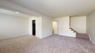 This two-floor residence offers a well-organized layout designed for comfortable everyday living. The main level features a generously sized living area finished with neutral-toned wall-to-wall carpeting, open white walls, and a staircase with a metal railing leading to the upper floor. Two windows allow natural light to fill the space, creating a bright and airy atmosphere. An open passageway connects the living area to the kitchen, which is outfitted with dark espresso-toned cabinetry, light marbled countertops, a stainless steel sink, and black appliances including a gas range and dishwasher, all set atop durable wood-style flooring. A dedicated laundry area on the main level includes a full-size washer and dryer with overhead cabinet storage for added convenience. The upper floor hosts multiple carpeted bedrooms, each featuring windows with natural views, closet access, and ceiling vents for climate control. The full bathroom is appointed with classic blue square tile surrounding the tub and shower, white mosaic tile flooring, and a wood-toned vanity. Throughout the space, the clean, neutral palette and practical layout provide a functional and move-in ready living environment.