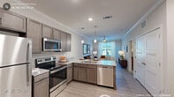 This single-story residence is thoughtfully designed with a modern aesthetic, combining functionality and comfort across its well-defined living spaces. The open-concept kitchen serves as a central feature, equipped with a full suite of stainless steel appliances, including a refrigerator, electric range, microwave, and dishwasher. Rich, taupe-toned cabinetry pairs with granite-style countertops, while pendant lighting illuminates a peninsula island that doubles as a breakfast bar with seating. Crown molding and recessed lighting elevate the kitchen's refined character.

The living area flows seamlessly from the kitchen, benefiting from natural light through large windows dressed with sheer curtains. Light wood-look flooring runs throughout the main living spaces, complementing the neutral gray walls and crown molding detail. A ceiling fan adds both practicality and style to the room.

The bedroom is carpeted for comfort, featuring multiple windows with blinds, a ceiling fan with light fixture, and ample space for furnishings. A walk-in closet provides generous storage.

The bathroom includes a dual-sink vanity with granite-style countertops, wood-toned cabinetry, and light wood-look flooring, maintaining the cohesive design language found throughout the residence.