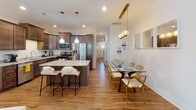 This two-floor residence offers a thoughtfully designed layout spread across two levels, beginning with a welcoming entryway that features warm hardwood flooring and a wood-railed staircase connecting both floors. The open-concept main level showcases a fully equipped kitchen with rich dark-stained cabinetry, granite countertops, stainless steel appliances including a gas range and built-in microwave, and a central island with bar seating. The kitchen flows seamlessly into a dining area adorned with elegant gold pendant lighting and a glass dining table, creating an ideal space for entertaining. The living area includes a tile-surround fireplace, hardwood floors, and stylish décor. A cozy secondary lounge area on the upper level features carpeted flooring and a tray ceiling, offering a more relaxed retreat. The bedrooms are comfortably sized with natural light from well-positioned windows. The bathrooms are finished with granite-topped dark wood vanities, large mirrors, and marble-tiled shower and tub surrounds. An additional half bath provides convenience. The property also includes an attached garage with an automatic door opener, completing this well-rounded and functional home.