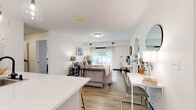This thoughtfully designed single-floor residence in Brewerton, NY offers a bright, open-concept living space with a seamless flow between the kitchen, dining, and living areas. Light wood-look flooring runs throughout, tying the spaces together with a clean, cohesive aesthetic.

The contemporary kitchen is a standout feature, showcasing white upper cabinetry, sage-toned lower cabinets, white quartz countertops, a classic subway tile backsplash, and stainless steel appliances including a refrigerator, range, and microwave. A peninsula with bar seating and pendant lighting adds both function and style.

The open living area is bright and welcoming, with natural light filtering through large windows dressed in sheer curtains. A dedicated dining space sits adjacent, completing the connected layout.

The bedrooms offer a calm, neutral palette with soft gray walls, natural light, and closet storage. Two bathrooms serve the residence: one featuring a granite-topped vanity, soaking tub, and large-format tile surround, and the other with a sleek glass-enclosed walk-in shower and matching matte black fixtures throughout.

Overall, the space presents a modern, move-in-ready design with consistent finishes, natural light, and a comfortable, well-organized floor plan.