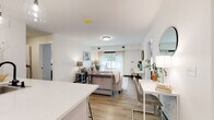 This thoughtfully designed single-floor residence in Brewerton, NY offers a bright, open-concept living space with a seamless flow between the kitchen, dining, and living areas. Light wood-look flooring runs throughout, tying the spaces together with a clean, cohesive aesthetic.

The contemporary kitchen is a standout feature, showcasing white upper cabinetry, sage-toned lower cabinets, white quartz countertops, a classic subway tile backsplash, and stainless steel appliances including a refrigerator, range, and microwave. A peninsula with bar seating and pendant lighting adds both function and style.

The open living area is bright and welcoming, with natural light filtering through large windows dressed in sheer curtains. A dedicated dining space sits adjacent, completing the connected layout.

The bedrooms offer a calm, neutral palette with soft gray walls, natural light, and closet storage. Two bathrooms serve the residence: one featuring a granite-topped vanity, soaking tub, and large-format tile surround, and the other with a sleek glass-enclosed walk-in shower and matching matte black fixtures throughout.

Overall, the space presents a modern, move-in-ready design with consistent finishes, natural light, and a comfortable, well-organized floor plan.