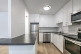 Located at 1001 Talwood Dr in Peterborough, Ontario, this 2-bedroom, 2-bathroom unit offers a clean, modern aesthetic throughout its thoughtfully designed single-floor layout. Light wood vinyl flooring flows seamlessly through the living spaces, complemented by crisp white walls and consistent flush-mount lighting.

The kitchen is a standout feature, showcasing white shaker-style cabinetry, a white subway tile backsplash, dark countertops, and a full suite of stainless steel appliances including a range, over-the-range microwave, dishwasher, and refrigerator. A peninsula counter connects the kitchen to the combined dining and living area, which benefits from a large floor-to-ceiling window dressed with vertical blinds, flooding the space with natural light.

Both bedrooms are well-sized, with the generously proportioned primary bedroom offering ample space. Each bedroom features light wood flooring, white walls, and baseboard heating. One bedroom includes dual windows with blinds, providing additional natural light.

The two bathrooms are finished with modern fixtures. One features a dark wood-toned vanity with a stone-look countertop and chrome hardware, while the other includes a bathtub/shower combination clad in classic white subway tile. A hallway with dedicated closet space completes the unit's practical layout.