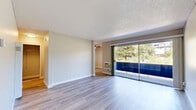 Located at 1250 Walker Ave in Walnut Creek, CA, this one-bedroom residence offers a clean, updated interior spread across a single floor. The living area is bright and open, finished with light-toned wood-style flooring that runs throughout the space. A full wall of sliding glass doors floods the room with natural light and provides direct access to a private balcony, framing pleasant views of surrounding greenery. A wall-mounted HVAC unit and a built-in floor heater ensure year-round climate comfort. Neutral-toned walls and a textured ceiling complete the living area's simple, functional aesthetic. The layout connects seamlessly to a secondary area, also featuring wood-style flooring and a tall built-in ventilation unit, providing additional flexibility. The bedroom offers a comfortable, quiet retreat with warm hardwood-style flooring, a window that invites natural light, and direct access to a bathroom featuring white cabinetry and vanity lighting. Throughout the space, crisp white baseboards and clean finishes create a cohesive, move-in-ready feel. A hallway provides practical connectivity between the home's spaces, rounding out a well-organized and efficiently designed floor plan ideally situated in the heart of Walnut Creek.