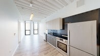 Located at 1135 N Sheridan in Chicago's Edgewater neighborhood, this single-floor unit showcases a contemporary design defined by striking exposed beam ceilings painted crisp white, which lend an industrial-modern character throughout the space. Light wood-style flooring runs continuously across the open layout, enhancing the sense of openness and flow.

The kitchen is appointed with two-tone cabinetry — warm gray lower cabinets paired with light upper cabinets — complemented by dark granite countertops and a coordinating backsplash. Stainless steel appliances include a professional-grade range with double oven, dishwasher, and refrigerator, making this a well-equipped cooking space.

The living area benefits from expansive floor-to-ceiling windows framed in bold black, inviting generous natural light and offering elevated views of the surrounding Edgewater cityscape and tree canopy. The bedroom mirrors this with dual large windows providing additional city views.

The bathrooms are finished with large-format neutral tile, featuring both a walk-in glass-enclosed shower and a separate soaking tub with sliding glass enclosure, complemented by light wood vanities topped with rich dark stone countertops.