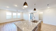 This two-story home offers a thoughtfully designed layout across two levels, with the majority of the living space situated on the upper floor. The ground level houses an attached garage equipped with an automatic opener, recessed lighting, and direct interior access via a hallway with warm hardwood-style flooring and staircase access to the main level above.

The upper floor centers around an open-concept kitchen and living room combination. The kitchen is well-appointed with warm-toned cabinetry, a subway tile backsplash, stainless steel appliances including a refrigerator, range, and microwave, and a large granite-topped island with an undermount sink and stylish pendant lighting. The adjoining living area benefits from multiple windows, a ceiling fan, and access to an outdoor balcony, creating a bright and airy atmosphere.

The three bedrooms are carpeted and fitted with ceiling fans, with windows providing natural light. The primary bedroom offers a comfortable footprint and closet access. The three bathrooms feature hardwood-style flooring, tiled tub-shower surrounds, and modern vanities. A dedicated laundry area accommodates a full-size washer and dryer side by side, adding everyday convenience to the home's functional layout.