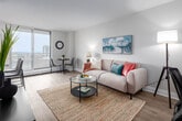 Located at 100 Forest Ave in Hamilton, Ontario, this well-appointed one-bedroom, one-bathroom unit offers a thoughtfully designed layout that maximizes every inch of its compact footprint. Light-toned luxury vinyl plank flooring flows throughout, lending a clean, cohesive look across all rooms.

The open-concept kitchen and living area forms the heart of the unit. The galley-style kitchen features white shaker cabinetry with brushed gold hardware, white quartz countertops, a subway tile backsplash, stainless steel appliances — including a built-in microwave, electric range, and refrigerator — and an undermount sink. A breakfast bar provides additional seating and connects seamlessly to the living area.

The living room is bright and airy, with a large floor-to-ceiling window that frames panoramic city views and floods the space with natural light. A dedicated dining nook sits adjacent to the window, making it ideal for everyday meals with a view.

The bedroom is a calm, comfortable retreat, featuring a generous window with cityscape views, a sliding closet, and neutral walls. The bathroom is finished with classic white subway tile surrounding a soaker tub and shower combination, with chrome fixtures throughout.

A hallway connects all rooms efficiently, completing this clean and modern urban residence.