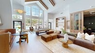 Located at 1400 El Camino Village Dr in Houston, Texas, this 3,210 square foot single-floor amenity space is thoughtfully designed to serve as a premier community gathering destination. The layout encompasses two living rooms, two kitchens, an exercise room, three bathrooms, and a hallway connecting the various areas.

The main living room is a showstopper, boasting soaring vaulted ceilings with exposed wooden beams, dramatic arched architectural details, and floor-to-ceiling windows that flood the space with natural light and offer views of the surrounding greenery and pool area. Light hardwood flooring runs throughout, complemented by warm, neutral tones. A billiards table anchors the room alongside plush seating arrangements.

A secondary lounge area with glass-panel doors provides a more intimate setting, featuring natural wood accents and an adjacent workspace. The two kitchens are outfitted with sleek, modern gray cabinetry, black hardware, white countertops, and light wood flooring, offering ample prep and storage space.

The dedicated exercise room is well-equipped with treadmills, ellipticals, rowing machines, and strength equipment, framed by large windows overlooking lush landscaping. The bathrooms feature elegant tilework, dark stone countertops, and modern fixtures, with one conveniently adjacent to the fitness center.