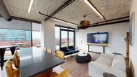 Located in Chicago's South Loop neighborhood, this party room offers a sophisticated and versatile gathering space defined by an industrial-chic aesthetic. The exposed concrete ceiling with visible ductwork and structural elements contrasts beautifully with clean white walls, while linear LED lighting and a statement brass pendant fixture provide warm, layered illumination throughout.

The open-plan layout is divided into distinct functional zones. A lounge area features teal upholstered seating, a sculptural textured ottoman, and a white sofa arranged around a large wall-mounted flat-screen TV, ideal for entertainment and casual mingling. A sleek dark-topped conference-style dining table surrounded by warm cognac leather chairs serves as a central gathering point, bathed in abundant natural light from floor-to-ceiling windows fitted with roller shades.

Panoramic views of the Chicago skyline are a defining feature, visible from multiple vantage points throughout the room. Glass doors open directly to an outdoor terrace, extending the entertaining space outside. A fully equipped kitchenette tucked toward the rear includes stainless steel appliances — a full-size refrigerator, dishwasher, and microwave — along with ample cabinetry and a sink, supporting catered or self-served events. The overall ambiance is modern, airy, and well-appointed, making this space well-suited for private events, social gatherings, and meetings alike.