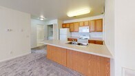 This single-floor unit at Harmony Heights in Rapid City, South Dakota offers a practical and well-organized layout designed for comfortable everyday living. The open-concept kitchen serves as a central hub, featuring warm honey-toned oak cabinetry extending to the ceiling for generous storage, light-toned countertops, and a peninsula with a double stainless steel sink that overlooks the adjacent living area. White appliances, including a refrigerator, electric range, and built-in microwave, provide a cohesive, clean aesthetic. Tile flooring runs throughout the kitchen and connecting hallways, offering durability and ease of maintenance.

The living areas are finished with plush wall-to-wall carpeting in a neutral gray tone, creating a warm, inviting atmosphere throughout. A door with a built-in blind provides direct outdoor access while allowing natural light to filter into the main living space. Ceiling fans with integrated light fixtures are featured in the bedrooms, enhancing comfort and airflow. At least one bedroom includes a sliding closet with built-in shelving, adding valuable storage. Windows offer views of the surrounding neighborhood, including mature trees, bringing a sense of connection to the outdoors. The overall color palette of crisp white walls and neutral finishes provides a clean, move-in ready environment.
