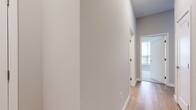 This single-floor residence offers a thoughtfully designed layout across two bedrooms and two bathrooms, finished with modern, neutral aesthetics throughout. Light hardwood flooring runs through the main living areas and kitchen, while plush carpet adds warmth to both bedrooms.

The kitchen serves as a functional centerpiece, featuring shaker-style cabinetry in a soft gray tone, quartz countertops with subtle veining, stainless steel appliances, and a central island with pendant lighting overhead. A window above the sink brings in natural light, enhancing the open, airy feel of the combined kitchen and living area.

The primary bedroom is a comfortable, naturally lit space with a large window and direct access to a dedicated walk-in closet equipped with wire shelving on both sides. Its en-suite bathroom includes a double-sink vanity with white cabinetry, matte black hardware, a large mirror, and a glass-enclosed tiled shower. The second bathroom features a clean white tub-shower combination with chrome fixtures and hardwood-style flooring.

The second bedroom, finished in the same neutral palette with carpeted floors, offers a quiet and versatile space. A connecting hallway with multiple doors provides efficient access to all rooms, maintaining a cohesive and functional flow throughout the unit.