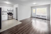 This two-bedroom, one-bathroom unit at 186 Thames Street in Chatham-Kent offers a thoughtfully arranged single-floor layout with a clean, contemporary aesthetic. The interior is finished in neutral grey and white tones throughout, complemented by smooth laminate wood flooring in the living and bedroom areas and light tile flooring in the kitchen.

The kitchen is efficiently designed with crisp white shaker-style cabinetry extending to the upper walls, a stainless steel range with overhead ventilation, a black refrigerator, and a single-basin sink. Light-reflecting tile flooring enhances the brightness of the space. The kitchen connects openly to the combined living area, creating a cohesive, easy-to-navigate layout.

The living room benefits from a large window and a door providing access to a balcony, allowing natural light to fill the space and offering an outdoor view of surrounding trees. The primary bedroom is a well-proportioned room with laminate flooring, neutral walls, and a closet. The second bedroom is similarly finished, providing a quiet and functional space.

The bathroom features a white vanity with an integrated sink, a large mirror, tile flooring, and a clean, minimal design. Overall, the unit presents a fresh, move-in-ready environment with consistent finishes throughout.