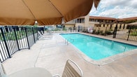 Situated at 1301 E Commonwealth Ave in Fullerton, California, this single-floor property offers a well-appointed outdoor living experience designed for comfort and community. The grounds are centered around a generously sized swimming pool with crystal-clear water, surrounded by a spacious concrete deck ideal for sunbathing and relaxation. A large shade canopy extends over a seating area poolside, providing relief from the Southern California sun while lounge chairs line the perimeter for guests to unwind. The pool area is enclosed by a secure iron fence, ensuring safety and privacy.

The courtyard serves as the social heart of the property, featuring a built-in BBQ station with multiple stainless steel grills set into a tiled masonry counter — perfect for outdoor gatherings and entertaining. The open-air courtyard is bordered by flowering plants and greenery, adding a welcoming touch of color to the paved surroundings.

The building itself presents a classic Spanish-inspired architectural style, characterized by a red tile roof, neutral stucco exterior, and covered walkway balconies. The surrounding landscape and accessible single-level layout contribute to a functional and inviting atmosphere, making this property a comfortable destination in the heart of Fullerton.