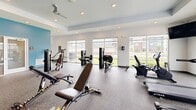 Located in Camby, Indiana, this fitness center offers a thoughtfully designed exercise space across a single open floor. The room is finished with durable speckled rubber flooring throughout, providing a safe and practical surface for a wide range of workouts. Accent walls painted in a calming teal/blue tone contrast with the crisp white walls and ceilings, creating an energizing yet clean aesthetic. A tray ceiling with recessed lighting adds architectural dimension overhead, while ceiling fans ensure comfortable air circulation during workouts.

Natural light floods the space through large floor-to-ceiling windows that line multiple walls, offering open views of the surrounding community grounds. The gym is well-stocked with a comprehensive selection of equipment, including multiple treadmills with individual monitors, stationary and recumbent bikes, a cable multi-functional training tower, and a range of Hoist strength machines targeting various muscle groups. A dedicated free weight section features a full dumbbell rack, adjustable benches, and additional functional training equipment. A wall-mounted television is positioned for easy viewing during cardio sessions. Mirrored wall panels further enhance the sense of openness. Glass-panel entry doors provide a welcoming, transparent entry point into this fully functional community fitness facility.