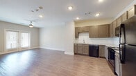 This single-floor unit offers a clean, modern design highlighted by warm hardwood-style flooring that flows consistently throughout every room. The open-concept layout seamlessly connects the living area to the kitchen, creating a spacious and functional environment. A ceiling fan anchors the living space, which benefits from natural light admitted through windows fitted with horizontal blinds.

The kitchen is thoughtfully designed with taupe-toned shaker-style cabinetry, sleek bar-pull hardware, and granite-look countertops. A classic white subway tile backsplash provides a crisp contrast to the cabinetry. Black appliances — including a refrigerator, electric range, over-the-range microwave, and dishwasher — are included. The sink area features a modern pull-down faucet for added convenience.

The bedroom is a generously sized, light-filled room with neutral walls and access to a walk-in closet equipped with a shelving system. The bathroom continues the consistent design language, featuring a framed sliding-glass shower enclosure with white tile surround, granite-look vanity countertop, and matching cabinetry. Recessed lighting throughout the unit ensures bright, even illumination in every space. The overall ambiance is clean, contemporary, and move-in ready.