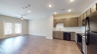 This single-floor unit offers a clean, modern design highlighted by warm hardwood-style flooring that flows consistently throughout every room. The open-concept layout seamlessly connects the living area to the kitchen, creating a spacious and functional environment. A ceiling fan anchors the living space, which benefits from natural light admitted through windows fitted with horizontal blinds.

The kitchen is thoughtfully designed with taupe-toned shaker-style cabinetry, sleek bar-pull hardware, and granite-look countertops. A classic white subway tile backsplash provides a crisp contrast to the cabinetry. Black appliances — including a refrigerator, electric range, over-the-range microwave, and dishwasher — are included. The sink area features a modern pull-down faucet for added convenience.

The bedroom is a generously sized, light-filled room with neutral walls and access to a walk-in closet equipped with a shelving system. The bathroom continues the consistent design language, featuring a framed sliding-glass shower enclosure with white tile surround, granite-look vanity countertop, and matching cabinetry. Recessed lighting throughout the unit ensures bright, even illumination in every space. The overall ambiance is clean, contemporary, and move-in ready.
