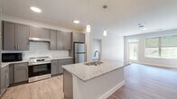 This well-appointed 2-bedroom, 2-bathroom residence in Rochester, MN offers a thoughtfully designed single-floor layout with modern finishes throughout. The open-concept kitchen serves as the heart of the home, anchored by a large granite-topped island with an undermount sink and stylish pendant lighting. Gray shaker-style cabinetry, a classic white subway tile backsplash, and stainless steel appliances — including a smooth-top range and full-size refrigerator — complete the contemporary kitchen aesthetic. Light wood-style plank flooring flows seamlessly from the kitchen into the living area, which benefits from natural light and direct access to an exterior door. Both bedrooms are comfortably sized, featuring neutral walls, large windows with exterior views of the surrounding greenery, and access to dedicated closets with built-in shelving. The primary bedroom connects to a spacious walk-in closet. The two bathrooms are finished with granite-topped gray vanities and brushed nickel fixtures; one features a walk-in shower with glass door, while the other includes accessibility-friendly grab bars for added convenience. Clean white walls, wide baseboards, and a consistent neutral palette give the entire residence a bright, cohesive, and move-in-ready feel.