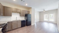 This well-appointed single-floor unit offers a clean, modern aesthetic with a thoughtful layout designed for comfortable everyday living. The kitchen is a standout feature, showcasing taupe shaker-style cabinetry, granite-look countertops, a white subway tile backsplash, and a full suite of black appliances including a refrigerator, electric range, built-in microwave, and dishwasher. The kitchen flows seamlessly into an open living area, which is bathed in natural light from large windows and equipped with a ceiling fan, creating a bright and airy atmosphere. Consistent light hardwood-style flooring runs throughout the entire unit, tying each space together cohesively. The bedrooms are generously sized, each featuring a ceiling fan, natural light from window blinds, and neutral walls that offer a calm, versatile backdrop. The unit includes two full bathrooms: one featuring a tiled shower-tub combination with a granite-topped vanity, and a second, more spacious bathroom with a walk-in tiled shower enclosed by a glass door and a wide double-sink vanity topped with granite. Both bathrooms continue the hardwood-style flooring and maintain the unit's consistent, polished design language throughout.