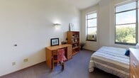 Located at 118 Prospect St in Ithaca, NY, this single-floor unit offers a practical and well-organized layout designed for efficient, comfortable living. The bedroom features wall-to-wall carpet, neutral-toned walls, and a tall window that allows natural light to fill the space while offering views of the surrounding greenery. Built-in wall sconce lighting complements the room, which also includes a wooden desk, bookshelf, and a single bed — providing a focused and functional living environment.

The kitchenette is thoughtfully equipped with cream-toned cabinetry, a coil-burner electric range, a microwave, a single-basin sink, a dishwasher, and a full-size refrigerator. The layout maximizes counter space along the walls, making the most of the compact footprint. A corridor with a rounded structural column connects the kitchen and bedroom areas, adding an architectural touch to the interior.

The bathroom is clean and straightforward, finished with light-toned walls and flooring. It includes a toilet and a shower enclosure with sliding glass doors, providing all essential amenities in a tidy, well-maintained space. Overall, the unit presents a no-frills, functional design well-suited for individual occupancy in the Ithaca area.