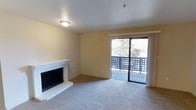 This single-floor residence offers three bedrooms and two bathrooms across a thoughtfully arranged floor plan. The living room serves as the heart of the home, highlighted by a white brick fireplace with a raised hearth that adds warmth and character to the space. Neutral-toned carpet extends throughout the living area, contributing to a soft and comfortable atmosphere. Warm yellow-beige walls complement the light color palette, creating a welcoming ambiance throughout.

A sliding glass door floods the living room with natural light and opens directly onto a private balcony enclosed by a decorative lattice railing, offering views of mature trees and the surrounding outdoor environment. The balcony provides an appealing extension of the living space, ideal for enjoying the outdoors.

The ceiling features a flush-mount light fixture, and a fire sprinkler is also present, reflecting practical safety considerations. The overall design is clean and straightforward, with a neutral finish palette that offers a versatile backdrop suitable for a variety of interior styles. The single-floor layout ensures convenient, accessible living throughout the entire home.