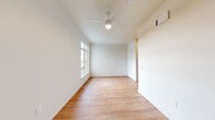 Located at 420 Center St NE in Salem, Oregon, this one-bedroom, one-bathroom unit offers a efficiently designed single-floor layout. The interior is finished with warm, light wood-tone hardwood-style flooring that runs consistently throughout the space, complementing the clean white walls and creating a bright, cohesive aesthetic.

The spacious primary bedroom is the largest room in the unit, occupying a generous portion of the total floor area. It features a ceiling fan with integrated lighting, a window that brings in natural light, and a louvered closet door for storage. The open, unobstructed layout of the bedroom provides flexibility for a variety of furniture arrangements.

A hallway connects the main living areas and leads to the bathroom, which is appointed with matte black fixtures and hardware, including towel bars and a toilet paper holder, adding a modern contrast to the white walls and light flooring. The hallway also provides access to what appears to be a kitchenette or kitchen area with cabinetry visible in the dollhouse overview.

The unit's overall design is clean and minimalist, with white walls, consistent flooring, and modern black accent hardware throughout. The layout is practical and well-organized, making efficient use of the available space. This unit is well-suited for individuals seeking a straightforward, move-in ready space in central Salem.