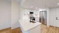 Located on the seventh floor at 1221-1331 S Eads St in Arlington, VA, this one-bedroom, one-bathroom unit offers a clean, modern aesthetic throughout. Warm hardwood-style flooring flows seamlessly across the entire living space, complementing the bright, neutral white walls and recessed lighting.

The open-concept kitchen is a standout feature, outfitted with crisp white cabinetry, a white quartz waterfall island with an undermount sink, and a full suite of stainless steel appliances including a gas range, over-the-range microwave, and a full-size refrigerator. The kitchen opens directly to the living area, creating a connected and functional layout ideal for everyday living and entertaining.

A hallway from the main living area leads to the generously sized primary bedroom, which features large floor-to-ceiling windows that invite natural light and offer views of the surrounding Arlington cityscape. The bedroom provides ample space for furnishing and personalization.

The bathroom is accessible from the hallway and includes a glass-enclosed shower, maintaining the unit's contemporary design language. The entry foyer provides a clean transition from the front door into the living spaces. Overall, this unit delivers a well-appointed, modern living experience in a prime Arlington location.