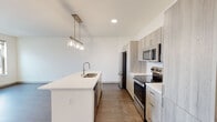 This single-floor unit presents a contemporary open-concept layout with a clean, modern aesthetic throughout. The kitchen serves as a central feature, showcasing light wood-tone cabinetry that extends floor to ceiling, a white quartz center island with a double-basin sink, and a full suite of stainless steel appliances including a refrigerator, electric range, and built-in microwave. A classic white subway tile backsplash adds texture, while pendant lighting above the island provides both task illumination and visual interest.

The living area flows seamlessly from the kitchen, offering an open and versatile space bathed in natural light. Sliding glass doors lead directly to a private balcony, extending the living space outdoors. Dark wood-finish flooring runs consistently throughout the unit, providing a warm contrast to the bright white walls and ceilings.

The bedrooms are well-proportioned, each featuring the same wood-finish flooring, neutral walls, and windows that allow natural light to filter in. Near the entryway, a large built-in closet provides generous storage. The overall ambiance is bright, clean, and contemporary, reflecting a thoughtfully designed modern living space.