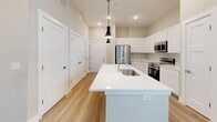 Located at 2901 Corporate Exchange Dr in Columbus, OH, this one-bedroom, one-bathroom unit offers a well-designed layout that maximizes its compact footprint. The open-concept kitchen serves as the centerpiece of the living space, showcasing crisp white shaker-style cabinetry extending to the ceiling, a large white quartz island with an undermount sink and pendant lighting, and a full suite of stainless steel appliances including a refrigerator, electric range, and built-in microwave. Light wood-look flooring flows throughout the kitchen and main areas, adding warmth to the neutral color palette. The bedroom features plush wall-to-wall carpeting, a ceiling fan, and a sliding glass door that opens directly onto a private balcony with outdoor views of the landscaped grounds. A dedicated closet provides convenient storage. The bathroom is clean and functional, offering a full tub-and-shower combination with built-in shelving, a white vanity, and matching light wood flooring. Neutral beige tones and recessed lighting throughout the unit create a bright, cohesive atmosphere that is both modern and move-in ready.