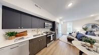 This single-floor studio is thoughtfully designed with a contemporary open-concept layout that seamlessly integrates the kitchen, living, and sleeping areas into one cohesive space. Light hardwood flooring runs throughout, lending warmth and visual continuity across every zone.

The kitchen is a standout feature, offering navy flat-front upper cabinets with gold hardware paired with dark wood-toned lower cabinetry and crisp white countertops. A tile backsplash, gold-finished faucet, stainless steel appliances — including a range, over-the-range microwave, French door refrigerator, and dishwasher — complete this functional and stylish space.

The living and sleeping area is bright and airy, benefiting from floor-to-ceiling windows that invite abundant natural light and provide views of the surrounding exterior. Recessed lighting and clean white walls enhance the open, uncluttered ambiance. A small dining area with bistro-style seating tucks neatly into the layout.

The bathroom features a glass-enclosed walk-in shower with large-format marble-look wall tiles, dark hexagonal floor tile, matte black fixtures, and built-in shelving — delivering a polished, spa-like aesthetic that complements the unit's overall modern character.