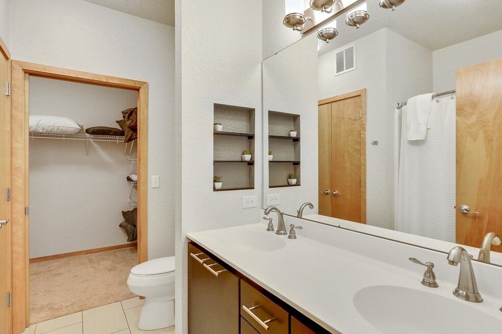 Modern bathroom with double vanity, toilet, and walk-in closet.