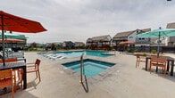 Located at 6205 Longstem Way in Loveland, Colorado, this outdoor community amenity space serves as a central gathering hub for its residential neighborhood. The centerpiece is a large, rectangular swimming pool with crystal-clear turquoise water, complemented by an expansive concrete pool deck outfitted with lounge chairs, chaise lounges, and colorful patio umbrellas for shade and relaxation.

Flanking the pool are several handsome wood pergola structures with slatted privacy screens, creating sheltered seating nooks that offer both shade and a sense of enclosure within the open-air setting. The pergolas are constructed with warm-toned timber framing that adds a natural, inviting aesthetic to the space.

Beyond the pool area, the amenity grounds include a well-maintained putting green, providing a recreational outlet alongside the aquatic facilities. Landscaped planting beds with young trees and ornamental grasses border the perimeter, softening the hardscape and adding greenery throughout. The entire area is enclosed by black metal fencing that defines the space while preserving views of the surrounding neighborhood homes, which feature contemporary farmhouse-style architecture with board-and-batten siding and metal roofing. The overall ambiance is clean, modern, and well-appointed, designed to foster outdoor community life.