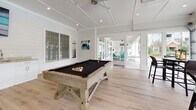 Located at 325 Marymeade Dr in Summerville, SC, this single-floor amenity space is thoughtfully designed for recreation and socializing. The interior is finished with crisp white shiplap walls, light hardwood-style flooring, and recessed lighting throughout, creating a bright and welcoming atmosphere.

The game room serves as a central gathering area, anchored by a rustic wood-framed billiard table with a dark felt surface. The open layout provides ample room for play and movement, while large glass-paned doors connect seamlessly to adjacent areas, enhancing the flow between spaces.

A well-appointed wet bar area features granite countertops, white cabinetry, a stainless steel sink, a beverage cooler, and a dedicated ice machine — all positioned beneath a wall-mounted television, making it an ideal entertainment hub.

The lounge area is defined by full-height glass panel garage doors that open completely to the outdoors, offering direct views of the community pool and surrounding greenery. A high-top dining table with seating is positioned to take full advantage of the indoor-outdoor connection, allowing natural light to flood the space and providing easy access to the pool deck.

Together, these areas form a versatile, resort-style community space well-suited for gatherings, leisure, and everyday amenity use.