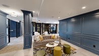 Located at 2811 S Cooper St in Arlington, Texas, this refined two-story commercial space blends classic architectural detailing with modern design sensibilities. The ground floor greets visitors with an elegant lounge area anchored by bold navy-blue wainscoting, decorative paneled columns, and large-format porcelain tile flooring. Plush tufted sofas, patterned area rugs, and curated accent seating create a welcoming, upscale atmosphere. Steel-framed glass partitions divide the open lounge from a private seating room, maintaining visual connectivity throughout. A dedicated conference room features an exposed brick accent wall, generous natural light from street-facing windows, a long communal table with ample seating, and a wall-mounted display screen, making it ideal for formal meetings. Distinctive wallpapered rooms with playful patterns add personality to the private office areas, each accessed through glass-paneled black doors. Wide, well-lit corridors with paneled wainscoting and herringbone tile inlays connect the various zones seamlessly. A staircase leads to the upper mezzanine level, where warm hardwood floors, an elegant chandelier, and an open-railing overlooking the floor below define the space. The upper level also offers a built-in high-top work table set against rich wood-paneled walls, perfect for focused collaboration or individual work.