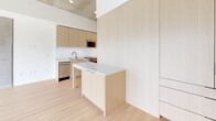 Located at 222 N City Dr in San Marcos, California, this thoughtfully designed single-floor unit offers a clean, contemporary aesthetic that maximizes every inch of its compact footprint. Light hardwood flooring runs throughout, complementing a neutral palette of whites and natural wood tones that give the space an open, airy feel.

The kitchen is a standout feature, equipped with sleek flat-front cabinetry in a warm wood finish, stainless steel appliances including a range, microwave, dishwasher, and refrigerator, and a stainless steel sink. A central island with a white countertop provides additional workspace and casual seating. A second kitchen area adds flexibility and functionality, making the space well-suited for various uses. An exposed concrete ceiling lends an industrial edge, while a large sliding glass door at the far end floods the space with natural light and offers views of the surrounding urban environment.

The bathroom features a clean, minimalist design with a full soaking tub framed by white subway tile, light wood open shelving for storage, hardwood flooring, and a toilet — all finished in a crisp, cohesive white-and-wood palette.

The entryway is clean and functional, with immediate access to the kitchen and living areas. Overall, the space presents a modern, efficient layout with high-quality finishes throughout.
