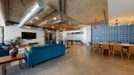 Located at 4061 Glencoe Ave in the vibrant Marina del Rey neighborhood of Los Angeles, this thoughtfully designed amenity space blends industrial aesthetics with modern comfort across a single, expansive floor. Exposed concrete ceilings with visible ductwork and structural columns give the space a raw, loft-like character, while polished concrete floors and warm wood accents create a refined, cohesive atmosphere throughout.

The open-plan layout features multiple distinct seating zones, including generous teal upholstered sofas and armchairs arranged around coffee tables and area rugs, offering flexible social and relaxation areas. A wall-mounted flat-screen TV anchors one lounge section, complemented by a well-stocked bookshelf unit in rich walnut tones. Floor-to-ceiling windows flood an additional lounge zone with abundant natural light and views of the surrounding neighborhood.

A glass-enclosed game room with a pool table provides a dedicated entertainment area, while a sleek kitchenette offers dark cabinetry, stainless steel countertops, a white subway tile backsplash, under-counter beverage refrigerators, and a microwave — ideal for hosting and gatherings. A dining area accented by bold geometric wallpaper and a contemporary chandelier completes the space with stylish flair.
