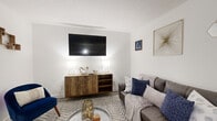 This two-story home offers a thoughtfully organized layout across two floors, combining comfortable living with practical design. The main level features a welcoming living area with light wood-style flooring, neutral white walls, and natural light streaming through multiple windows with blinds. The kitchen is efficiently designed with white cabinetry, white appliances including a refrigerator and range, and wood-look flooring that ties the space together cleanly. A hallway connects the main living areas, and two staircases provide convenient access between floors. The upper level hosts the three bedrooms and two full bathrooms. The generously sized primary bedroom features plush carpeting, a ceiling fan, dual windows for natural light, and ample floor space for comfortable furnishing. The two additional bedrooms are well-proportioned, each with carpet flooring, ceiling fans, closets with louvered doors, and windows that bring in natural light — ideal for a variety of uses. Both bathrooms are clean and functional, each featuring a tub-shower combination and vanity with storage. Throughout the home, the consistent use of white walls, neutral tones, and a mix of hard and soft flooring surfaces creates a cohesive, modern aesthetic.