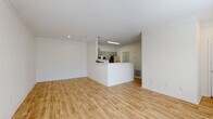 This single-floor unit is defined by a bright, cohesive aesthetic, with light hardwood-style flooring running consistently throughout every room. The open-concept living area is generously proportioned, featuring white walls, crown molding, and a smooth ceiling that together create a clean, airy atmosphere. Natural light filters in through windows fitted with blinds, enhancing the sense of openness.

The kitchen is positioned at the heart of the unit, anchored by a wraparound peninsula that provides both workspace and a casual dining option. Gray shaker-style cabinetry lines the walls, complemented by a light stone-finish countertop, a stainless steel sink, and a full suite of stainless steel appliances including a refrigerator, electric range, and over-the-range microwave. A dedicated laundry room houses a full-size washer and dryer and includes wire shelving for added storage.

The bedroom is well-sized with a window offering outdoor views and access to a walk-in closet. The bathroom features a combined tub and shower with white tile surround, a gray vanity with a stone-finish countertop, and matching hardwood-style flooring. Throughout the unit, the consistent finishes and neutral palette create a modern, functional, and welcoming living environment.
