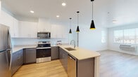 This well-appointed single-floor residence showcases a clean, modern design throughout. The kitchen serves as the heart of the space, featuring a two-tone cabinet scheme with crisp white upper cabinets and slate-gray lower cabinets, complemented by light quartz countertops. A generous kitchen island with an undermount sink anchors the space, while three striking black cone-shaped pendant lights add a bold design accent overhead. Stainless steel appliances, including a refrigerator, electric range, over-the-range microwave, and dishwasher, complete the fully equipped kitchen. Light-toned hardwood flooring flows seamlessly from the kitchen into the open-concept living area, creating a bright and cohesive atmosphere. Recessed lighting and natural light from well-positioned windows contribute to the airy feel of the main living spaces. The bedrooms feature plush carpeting and windows with views to the exterior. The bathrooms are finished with gray vanities topped with light quartz countertops, undermount sinks, brushed nickel fixtures, and full tub-shower combinations. A dedicated in-unit laundry closet houses a side-by-side Whirlpool washer and dryer, adding a practical and convenient touch to everyday living.