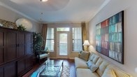 Located at 5960 Siegen Ln in Baton Rouge, Louisiana, this single-story residence offers a thoughtfully designed layout with a warm, welcoming ambiance throughout. The living room serves as the heart of the home, showcasing rich hardwood flooring, crown molding, and an abundance of natural light streaming in through large windows and a glass-paneled exterior door framed by elegant drape panels. A glass-top coffee table and built-in shelving add functional style to the space.

The kitchen is efficiently arranged with warm wood cabinetry extending to the ceiling, stainless steel appliances including a refrigerator, dishwasher, and range, and a breakfast bar that connects seamlessly to the living and dining areas. Hardwood flooring continues throughout, lending a cohesive feel to the common spaces.

The bedroom is a serene retreat, carpeted for comfort and fitted with a ceiling fan, a generous window with outdoor views, and neutral wall tones that create a calm atmosphere. Decorative leaf-motif wall art adds a distinctive, nature-inspired touch.

The bathroom features hardwood flooring, an extended dual-sink vanity with ample counter space, a soaking tub, and a walk-in closet, providing both practicality and comfort. Overall, the space is characterized by consistent finishes, natural light, and a clean, inviting aesthetic.