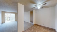 This single-floor unit offers three bedrooms, one bathroom, and a practical layout across a modest but efficiently arranged footprint. The living area features neutral-toned carpet, a textured popcorn ceiling, and a ceiling fan with integrated light fixture, with tile flooring marking the transition toward the kitchen. A sliding glass door or large vertical window treatment allows natural light to fill the open living space.

The kitchen is equipped with a coil-top electric range, dishwasher, and wood-toned cabinetry, complemented by tile flooring and a window overlooking greenery outside. A hallway connects the bedrooms and bathroom, providing clear circulation throughout the unit.

Each bedroom features wall-to-wall carpet, textured ceilings, and built-in closets with hanging rods. The primary bedroom includes a double-door closet and a window with blinds admitting natural light. Additional bedrooms also include single closets and windows. Baseboard heating units are present in the bedrooms.

The bathroom includes a full tub-shower combination with a white surround, a wood-framed vanity mirror, granite-style countertop, and wood-look vinyl flooring, presenting a clean and functional design throughout.
