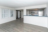 Located at 17457 Manderson Rd in Detroit, Michigan, this single-floor residence offers a well-designed layout that balances modern updates with functional living. The open-concept living and dining area is anchored by rich dark hardwood flooring that flows throughout much of the unit, complemented by neutral gray walls that create a clean, contemporary backdrop. A set of French doors with vertical blinds invites natural light into the living space while providing access to the outdoors. An elegant arched doorway adds a classic architectural touch, connecting the main living area to additional rooms. The kitchen features a galley-style configuration with dark wood-grain cabinetry, bold blue countertops, stainless steel appliances including a refrigerator and microwave, and track lighting overhead — combining practicality with modern style. A peninsula counter opens the kitchen toward the living space, enhancing the open feel. The bedroom is finished with plush carpeting, a ceiling fan, a wall-mounted HVAC unit, and a window dressed with vertical blinds for natural light and privacy. The bathroom is distinctively styled with dark square tile wainscoting, yellow-green upper walls, a white vanity with mirror, and a window that brings in natural light.