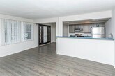 Located at 17457 Manderson Rd in Detroit, Michigan, this single-floor residence offers a well-designed layout that balances modern updates with functional living. The open-concept living and dining area is anchored by rich dark hardwood flooring that flows throughout much of the unit, complemented by neutral gray walls that create a clean, contemporary backdrop. A set of French doors with vertical blinds invites natural light into the living space while providing access to the outdoors. An elegant arched doorway adds a classic architectural touch, connecting the main living area to additional rooms. The kitchen features a galley-style configuration with dark wood-grain cabinetry, bold blue countertops, stainless steel appliances including a refrigerator and microwave, and track lighting overhead — combining practicality with modern style. A peninsula counter opens the kitchen toward the living space, enhancing the open feel. The bedroom is finished with plush carpeting, a ceiling fan, a wall-mounted HVAC unit, and a window dressed with vertical blinds for natural light and privacy. The bathroom is distinctively styled with dark square tile wainscoting, yellow-green upper walls, a white vanity with mirror, and a window that brings in natural light.