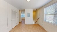 Located at 1100 E Washington Ave in East Point, Georgia, this two-story, 2-bedroom, 1-bathroom unit offers a practical and well-appointed layout. Entry is made through a ground-level foyer with painted cinder block walls and a tiled staircase with a wood handrail leading up to the main living level. The upper floor encompasses the majority of the living space and is finished with light wood laminate flooring throughout, creating a bright and cohesive feel.

The kitchen is a standout feature, outfitted with crisp white shaker-style cabinetry, black hardware accents, light countertops, and a full suite of stainless steel appliances including a gas range, microwave, dishwasher, and refrigerator. A large window fills the kitchen with natural light. The open hallway area includes an electrical panel and louvered closet door, providing practical storage access.

Both bedrooms feature painted cinder block walls, light wood flooring, and ceiling fans with integrated lighting. The primary bedroom is a comfortable size and benefits from natural light through a window with blinds. The bathroom is cleanly finished with white subway tile in the tub/shower surround, mosaic tile flooring, a white vanity with a single sink, and matte black fixtures throughout.